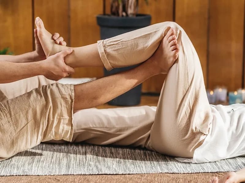 A practitioner holding a recipient's feet during a lying-down Thai Yoga stretch